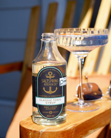 SaltSpring Kitchen Company - Classic Tonic Syrup with a cocktail glass on a chair outside