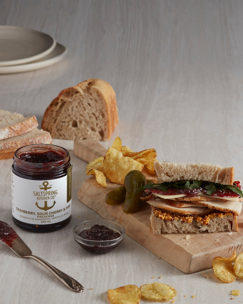 Sandwich with chips and a jar of preserves on a wooden board