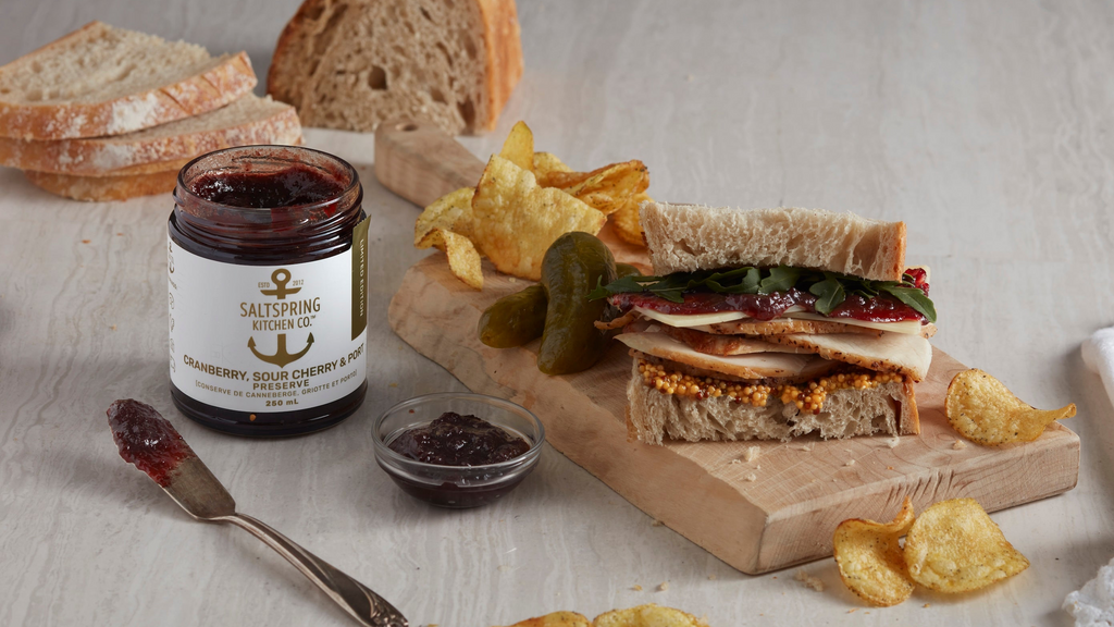 Sandwich with chips and a jar of preserves on a wooden board 