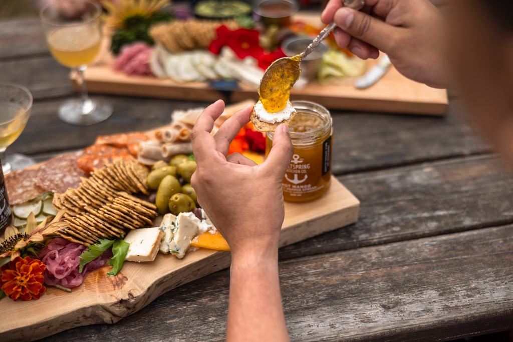 Person spreading jam on crack with a charcuterie board in the background