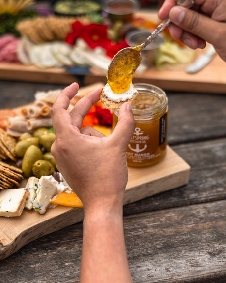 SaltSpring Kitchen Company Hot Mango Spicy Pepper Spread on a spoon with a charcuterie board