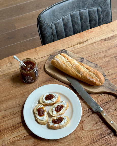 Bread with jam on a plate, jar of jam, and knife on a wooden table.