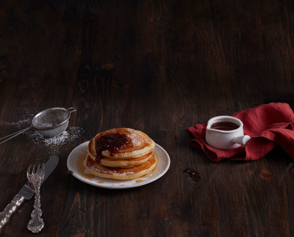 Stack of pancakes with Raspberry and Rose Fruit Spread and syrup on a plate on a wooden table.