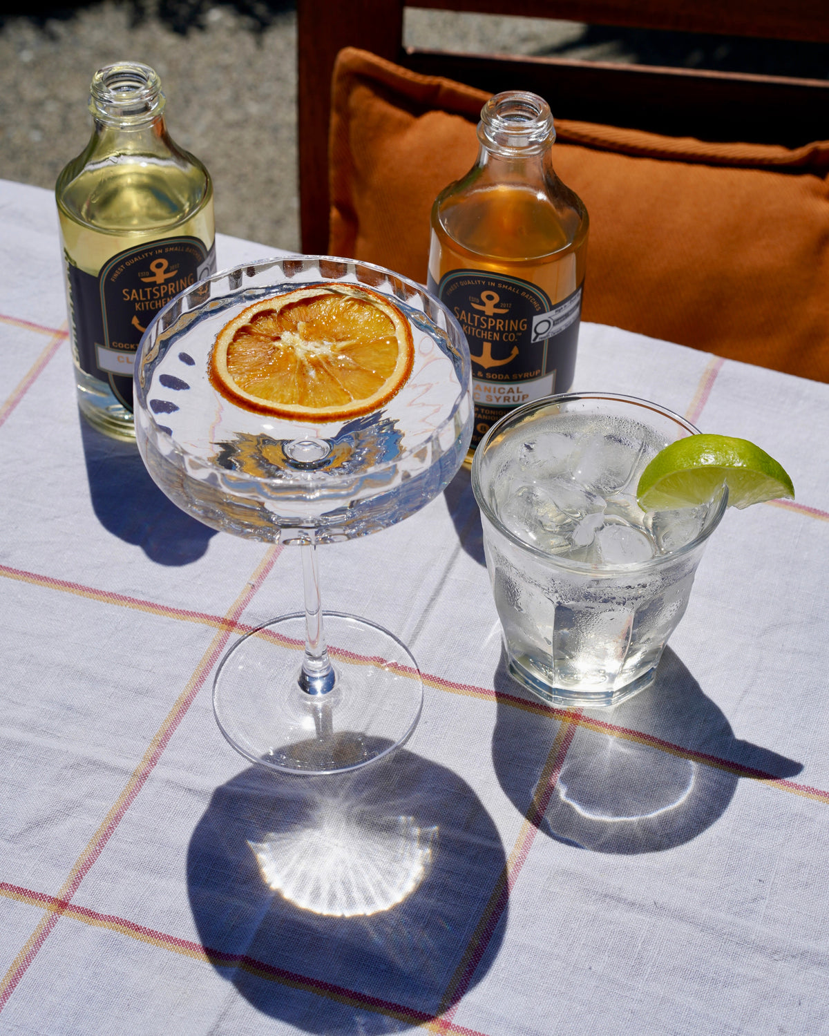 SaltSpring Kitchen Company Tonic Syrups with mocktails on a table outside with a lime wedge and orange slice garnish