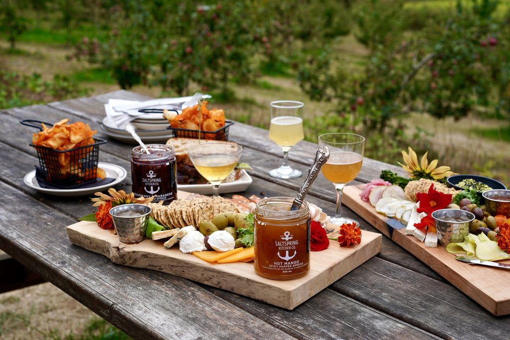 Outdoor setting with a wooden table featuring a charcuterie board, drinks, and snacks.